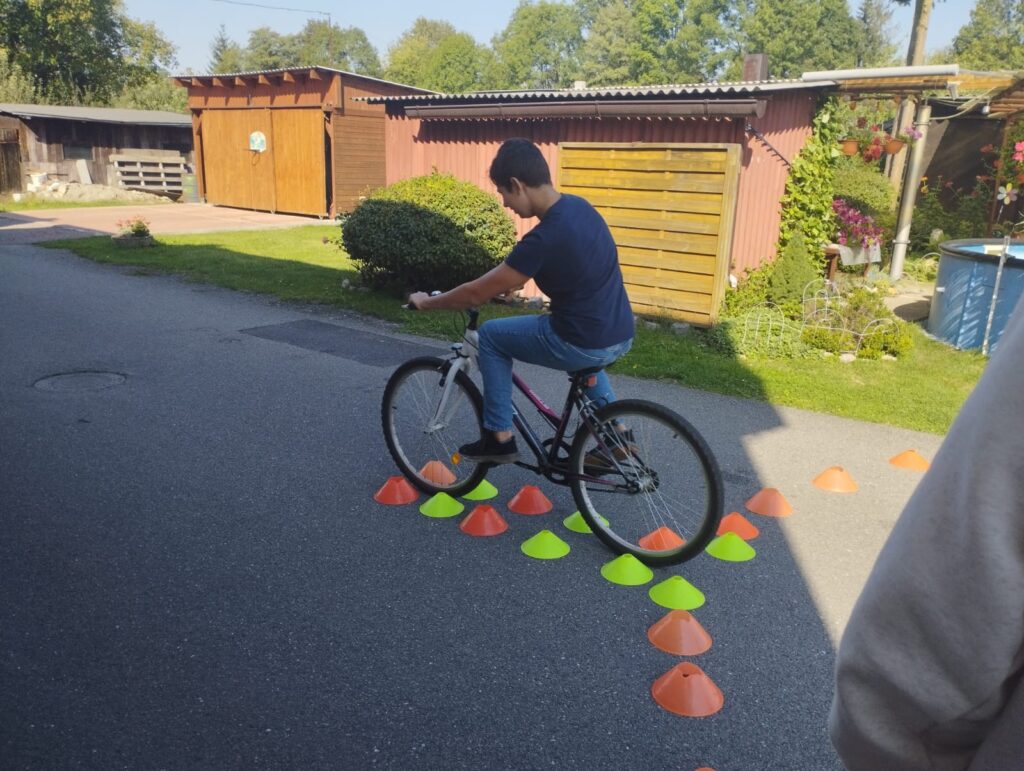 žák na kole jedoucí úzkou cestou vyznačenou z kuželů